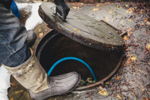 Worker wearing gloves lifting a metal sewer hatch cover on the street